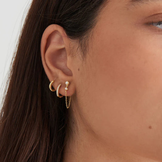Close-up of an ear with gold earrings against a neutral background