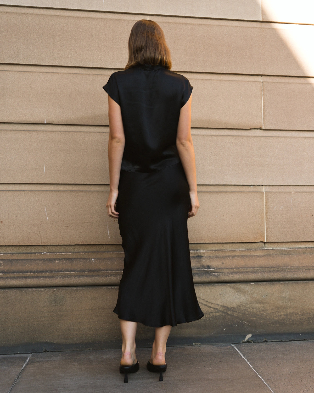 Woman wearing a black dress standing against a beige wall.