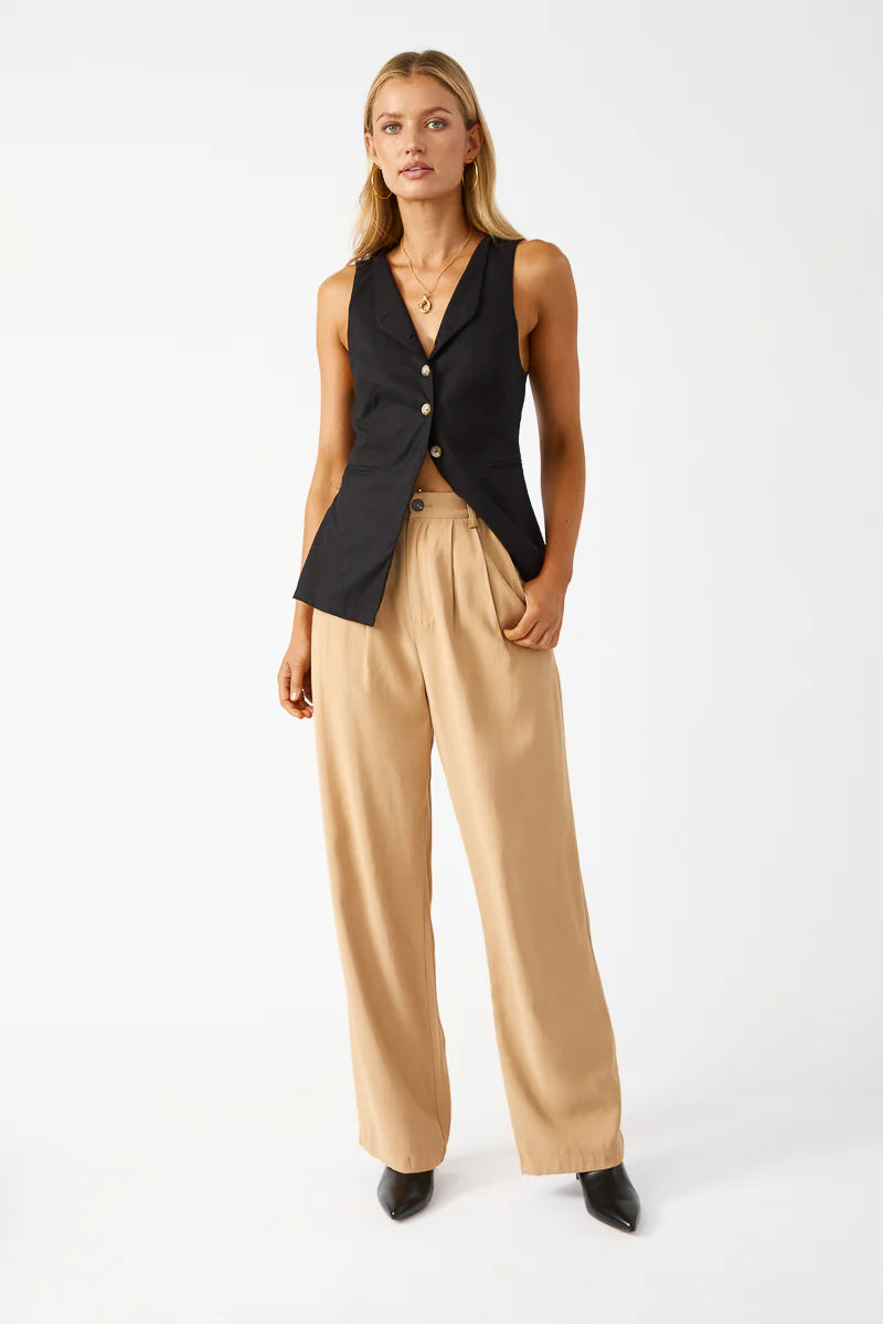 Woman wearing a black sleeveless blazer and beige pants on a white background