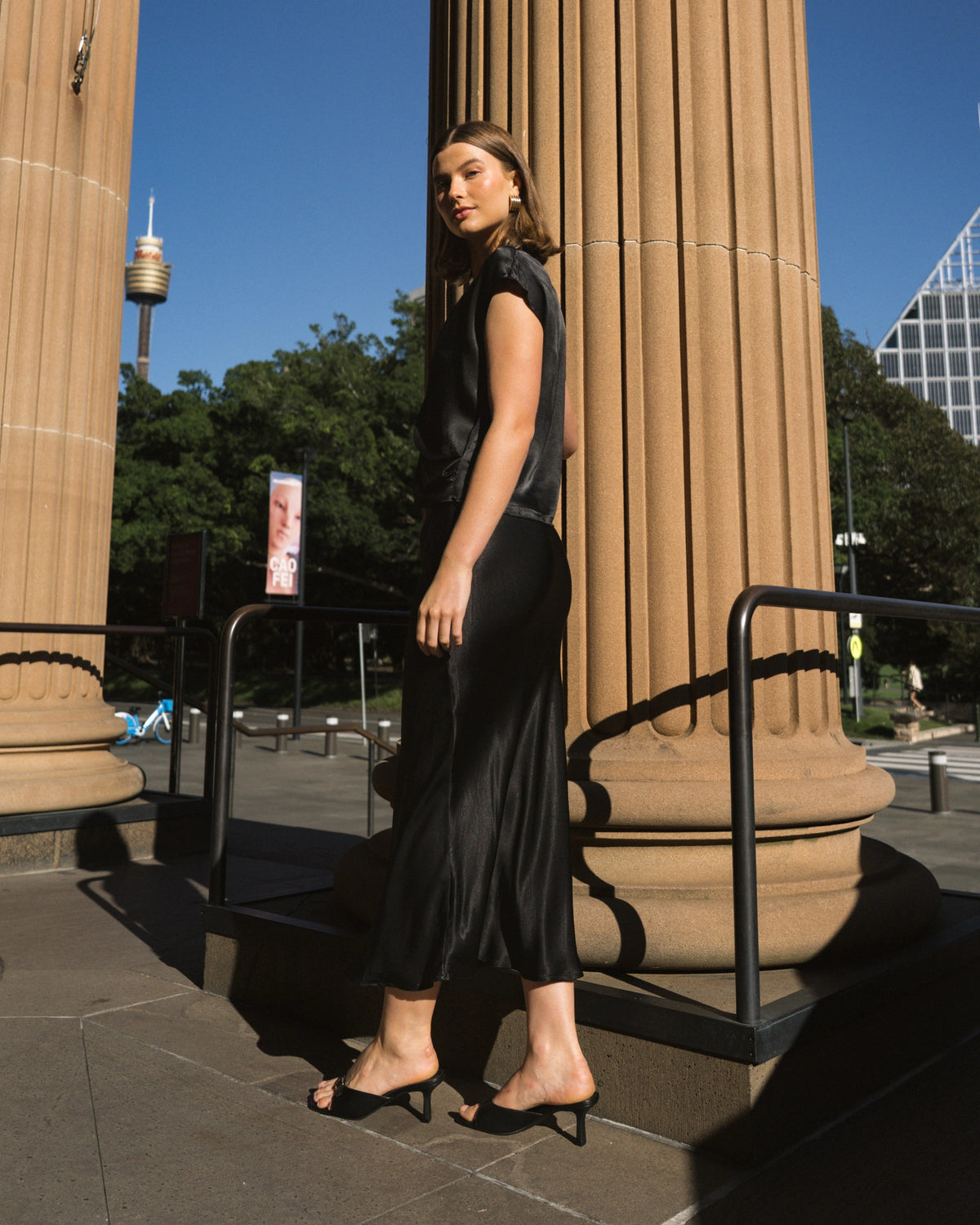 Woman in a black dress standing between two large columns with a cityscape in the background